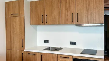 Moderne Küchenzeile mit Holzfronten, weißer Arbeitsplatte, Induktionskochfeld und integriertem Backofen.