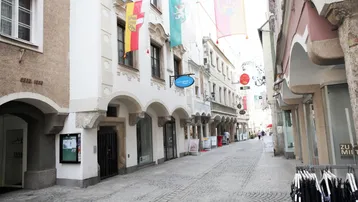 Historische Gasse mit Kopfsteinpflaster, alten Gebäuden und bunten Flaggen in einer belebten Stadt.