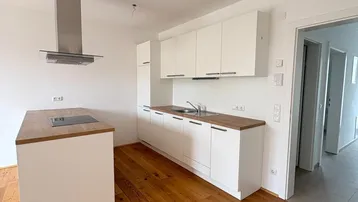 Moderne Küche mit weißen Schränken, Holz-Arbeitsplatte und Kochinsel mit Induktionskochfeld.