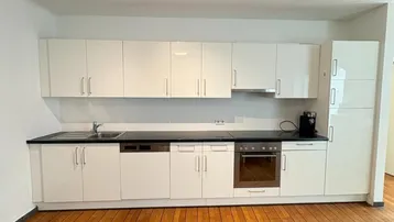 Moderne Einbauküche mit weißen Hochglanzfronten, dunkler Arbeitsplatte und Holzboden.