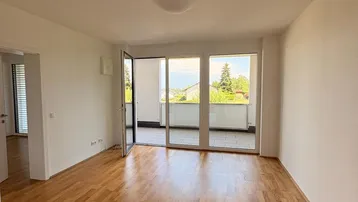 Helles Wohnzimmer mit Parkettboden, weißen Wänden und Zugang zu einem Balkon mit grüner Aussicht.