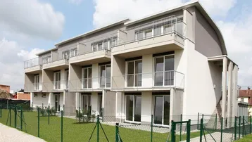 Modernes Mehrfamilienhaus mit Balkonen und kleinen Gärten im Erdgeschoss, umgeben von einer Grünfläche.