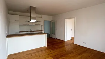 Heller offener Wohn-Essbereich mit moderner Einbauküche und Holzboden.