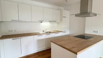Moderne Küche mit weißen Schränken, Holzarbeitsplatten, Kochinsel und Dunstabzugshaube.