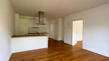 Heller offener Wohn-Essbereich mit moderner Einbauküche und hochwertigem Holzfußboden.