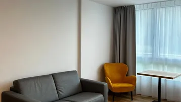 Helles Wohnzimmer mit Holzboden, einem grauen Sofa und einem gelben Sessel am Fenster.