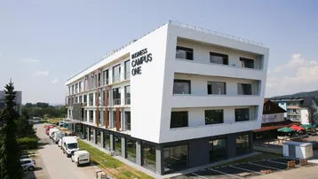 Modernes Geschäftsgebäude mit weißer Fassade, großen Fenstern und Parkplätzen unter blauem Himmel.