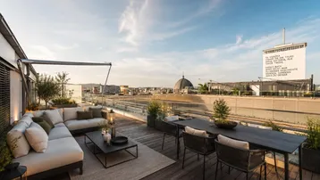 Geräumige Dachterrasse mit modernen Lounge-Möbeln, Esstisch und weitem Stadtblick unter blauem Himmel.