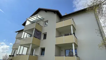 Modernes Mehrfamilienhaus mit mehreren Balkonen und einem verglasten Wintergarten unter blauem Himmel.