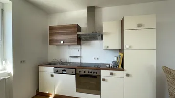 Helle Küche mit Einbaugeräten, Parkettboden und Fenster für Tageslicht.