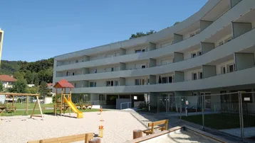 Modernes Wohngebäude mit zahlreichen Balkonen und einem Spielplatz im Außenbereich.