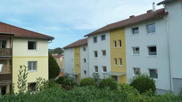 Mehrere Wohngebäude mit gelben und weißen Fassaden sowie roten Ziegeldächern, umgeben von grünen Hecken.