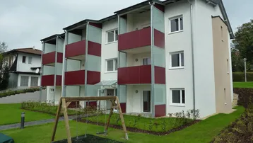 Modernes Mehrfamilienhaus mit Balkonen, gepflegter Rasenfläche und Kinderspielplatz im Vordergrund.