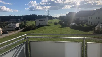 Sonniger Ausblick vom Balkon über grüne Wiesen und ländliche Umgebung mit Häusern.
