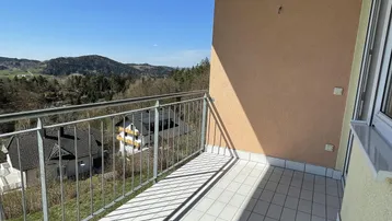 Sonniger Balkon mit Fliesenboden, Metallgeländer und weitem Blick über die Landschaft.