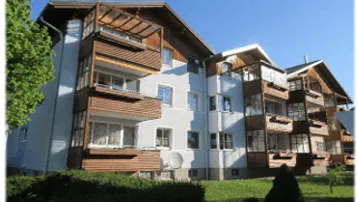 Modernes Mehrfamilienhaus mit Holzverkleidungen an den Balkonen und gepflegter Grünfläche im Vordergrund.