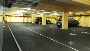 Tiefgarage mit mehreren Stellplätzen, gelben Säulen und sichtbaren Installationen an der Decke.