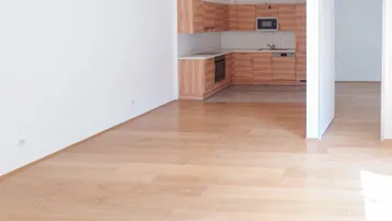 Helles Zimmer mit Holzboden und offener Küche, ideal für einen kombinierten Wohn- und Essbereich.