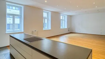 Heller offener Wohnbereich mit moderner Kücheninsel, Holzboden und vielen Fenstern für natürliches Licht.
