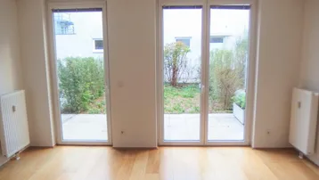 Heller Wohnraum mit Holzboden und großen Fenstertüren, die zu einem kleinen Gartenbereich führen.