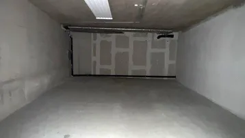 Ein leerer, unfertiger Lagerraum im Kellergeschoss mit Betonwänden, sichtbaren Leitungen und Deckenbeleuchtung.
