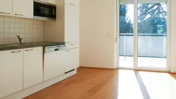 Helle Küche mit weißen Schränken, integrierten Geräten und Zugang zu einem sonnigen Balkon.