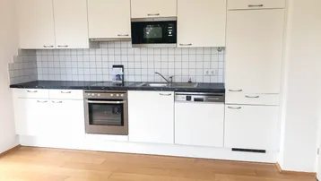 Moderne Einbauküche mit weißen Schränken, dunkler Arbeitsplatte und integrierten Geräten.