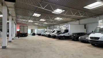 Geräumige Lagerhalle mit hoher Decke, Oberlichtern und mehreren geparkten Lieferwagen.