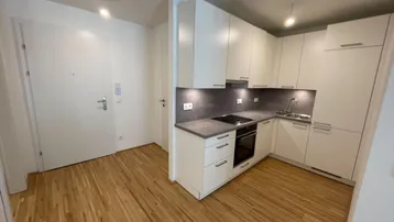 Moderne Einbauküche mit weißen Schränken, dunkler Arbeitsplatte und Holzboden in einem offenen Bereich.