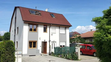 Modernes Einfamilienhaus mit rotem Ziegeldach, weiß-grauer Fassade und gepflegtem Vorgarten.