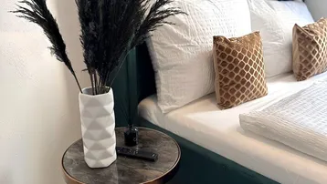 Gemütliches Schlafzimmer mit modernem grünen Bett, stilvollem Nachttisch und dekorativer Pampasgras-Vase.