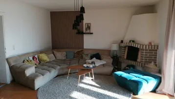 Gemütliches Wohnzimmer mit großem Ecksofa, Kamin und Holzboden, hell durchflutet.