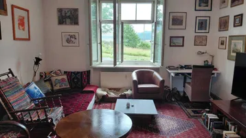Gemütliches Wohnzimmer mit Teppichboden, vielen Bildern und einem weiten Blick ins Grüne.