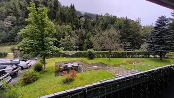Blick vom Balkon auf den Gartenbereich mit Sitzgelegenheiten und die umliegende Berglandschaft.