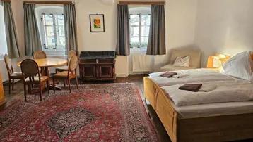 Gemütliches Schlafzimmer mit traditionellem Teppich, zwei Fenstern und einem kleinen Essbereich.