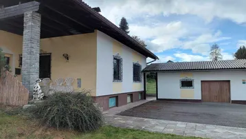 Hausfassade mit angrenzender Garage und gepflegtem Vorgarten unter bewölktem Himmel.