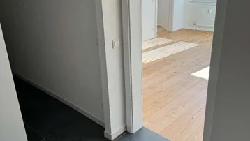 Heller Flur mit dunklen Fliesen und Blick in ein sonniges Zimmer mit Holzfußboden.