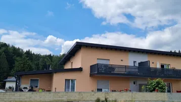 Modernes Wohnhaus mit Balkon und Blick ins Grüne unter blauem Himmel.