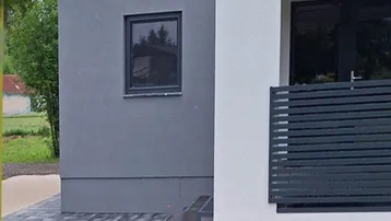 Moderne Gebäudefassade mit weißem und grauem Putz sowie einem kleinen Fenster.