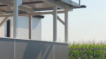 Außenansicht des Gebäudes mit überdachtem Bereich und Satellitenschüssel vor ländlicher Kulisse.