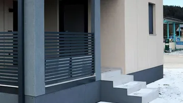 Moderne Gebäudefassade mit überdachtem Eingangsbereich und Treppe im Schnee.