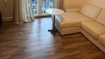 Helles Wohnzimmer mit beigem Ecksofa, Holzboden und Zugang zu einem Balkon oder einer Terrasse.