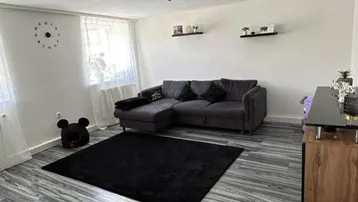 Gemütliches Wohnzimmer mit modernem Laminatboden, bequemer Eckcouch und viel Tageslicht.