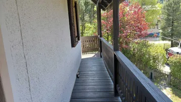 Langer Holzbalkon mit Geländer und Blick auf die umliegende Natur und eine ruhige Straße.