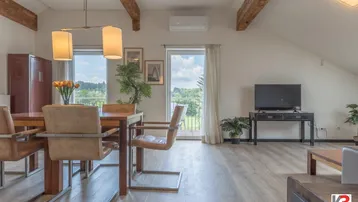 Heller Wohn- und Essbereich mit Holzbalken, Parkettboden und Zugang zu einem Balkon mit grüner Aussicht.