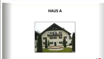 Traditionelles Haus mit Giebeldach, Balkonen und gepflegtem Vorgarten mit Zierbäumen.