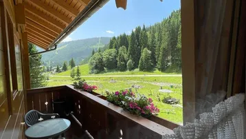 Balkon mit Holzboden und Sitzgelegenheiten, bietet einen weiten Blick auf die grüne Berglandschaft.