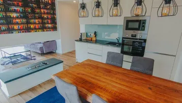 Moderner offener Wohn- und Essbereich mit integrierter Küche, Holztisch und farbenfroher Wandkunst.