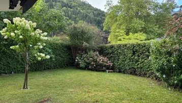 Gepflegter Gartenbereich mit Rasenfläche, hohen Hecken und Blick auf die bewaldeten Hügel.