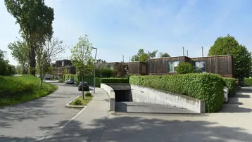 Moderne Holzfassadenhäuser mit Tiefgaragenzufahrt und grüner Hecke in einer Wohnsiedlung.